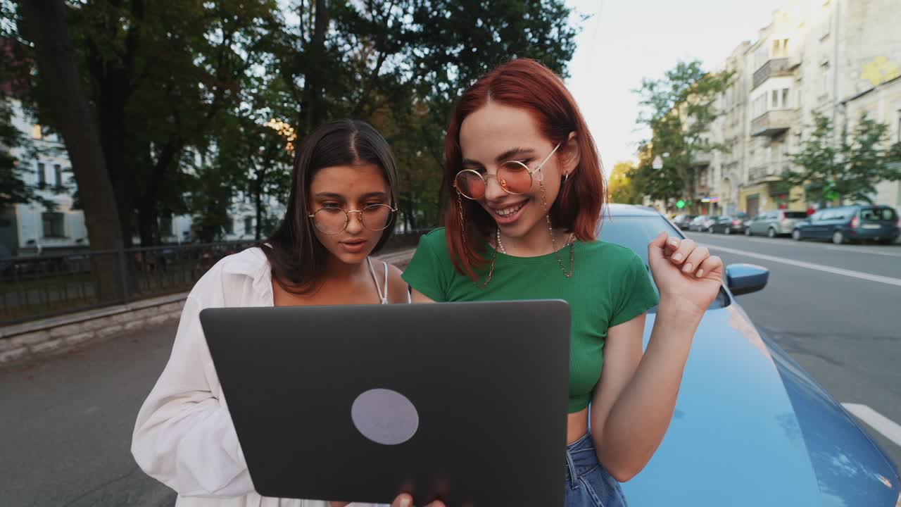 dos mujeres jóvenes mirando una computadora portátil al aire libre