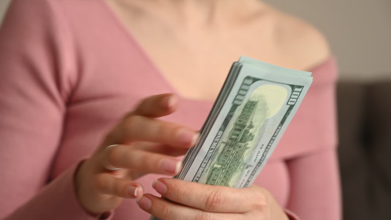 Smiling woman counting multiple one hundred dollar bills in her hands