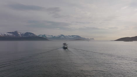 Ferry-sailing-towards-snowy-mountains-on-Senja-Island,-Norway