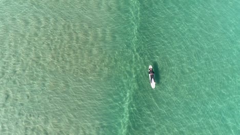 vista aérea superior de un hombre acostado y descansando en su tabla de surf en el agua mientras una ola rueda debajo de él