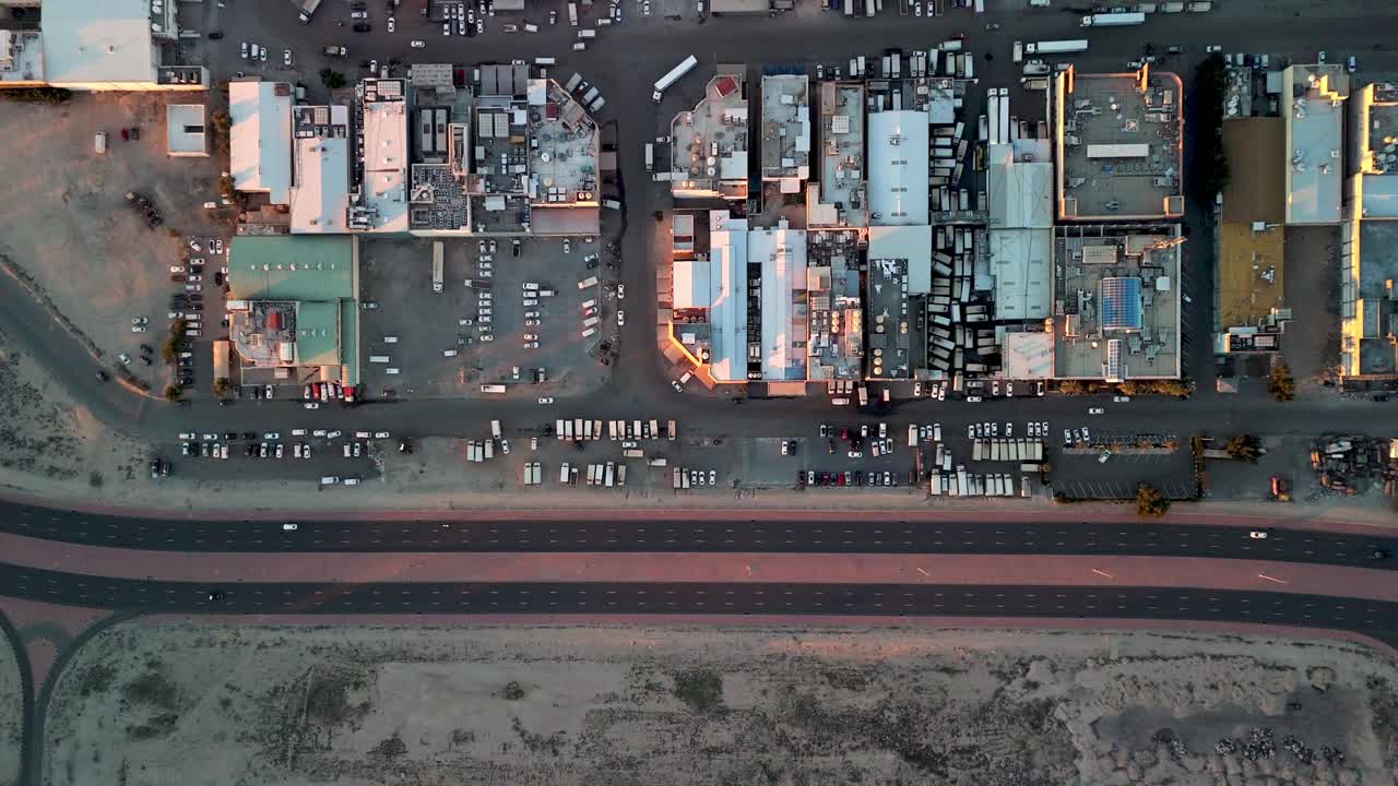 Vertikale Drohnenaufnahme eines industriellen Lagerhausbezirks mit LKW, Parkplätzen und Autobahnverkehr. Warmes Sonnenuntergangslicht über den Wüstenstadtrand und die Logistikinfrastruktur