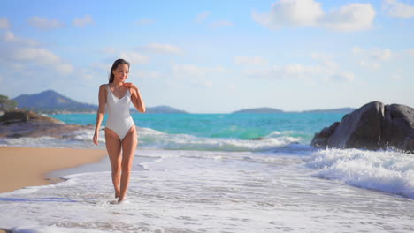 Bella-Mujer-En-Traje-De-Baño-Caminando-Alegremente-En-Una-Playa-Exótica,-Rastreando