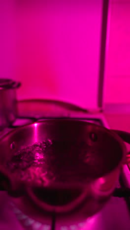 pot of water boiling on a gas stove, illuminated by pink light