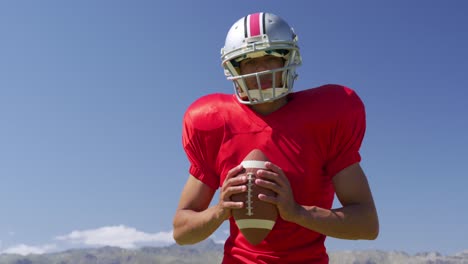 American-football-player-standing-with-helmet-and-rugby-ball