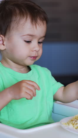 pretty caucasian boy eating from fork which he's holding in left hand. mom puts the fork into son's right hand and helps him to take some food. vertical video