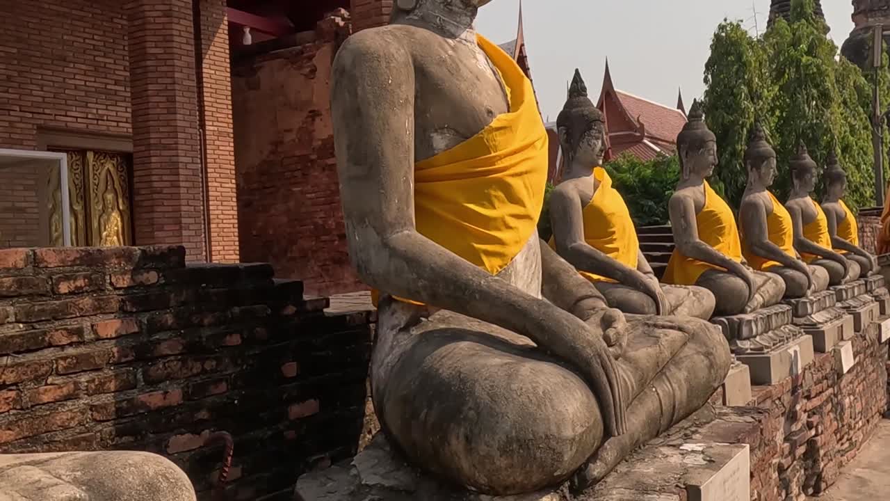 A close-up view of seated Buddha statues adorned with yellow robes against a backdrop of brick walls.