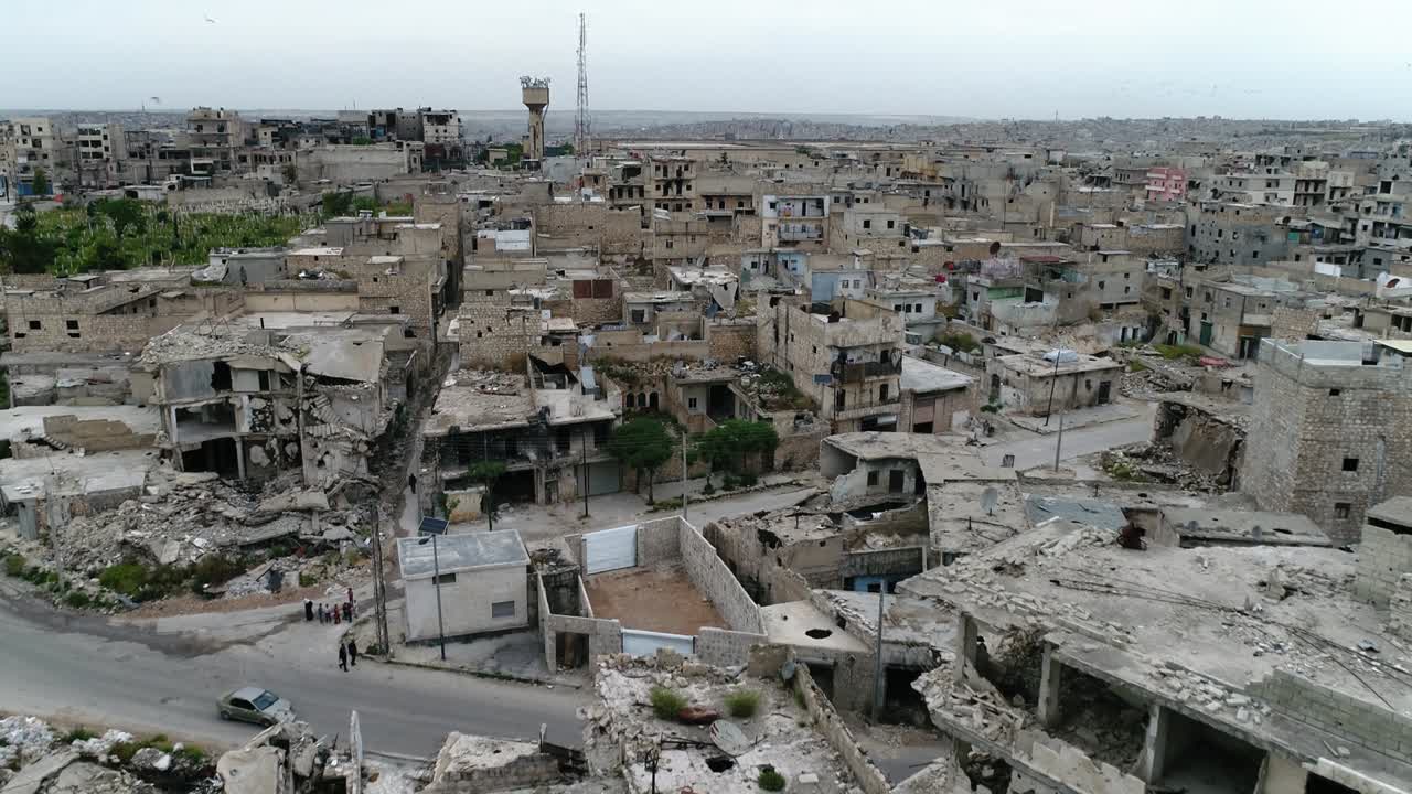 estradas de uma cidade síria com carros dirigindo em uma estrada e pessoas caminhando. alguns dos edifícios ainda estão em ruínas após a guerra civil há 10 anos - vista aérea com um drone 4k