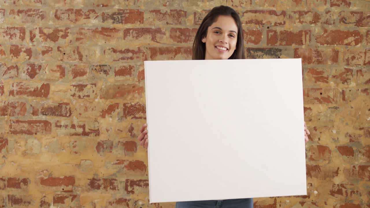 Caucasian woman holding a white rectangle on a brick wall