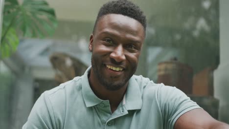 retrato de un feliz hombre afroamericano sentado y mirando a la cámara en el jardín