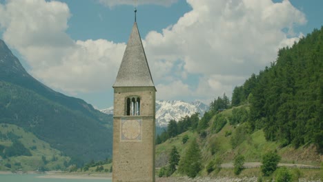 medium shot, scenic view of kirchturm von altgraun on the lake of reschensee in italy, mountain range in the background