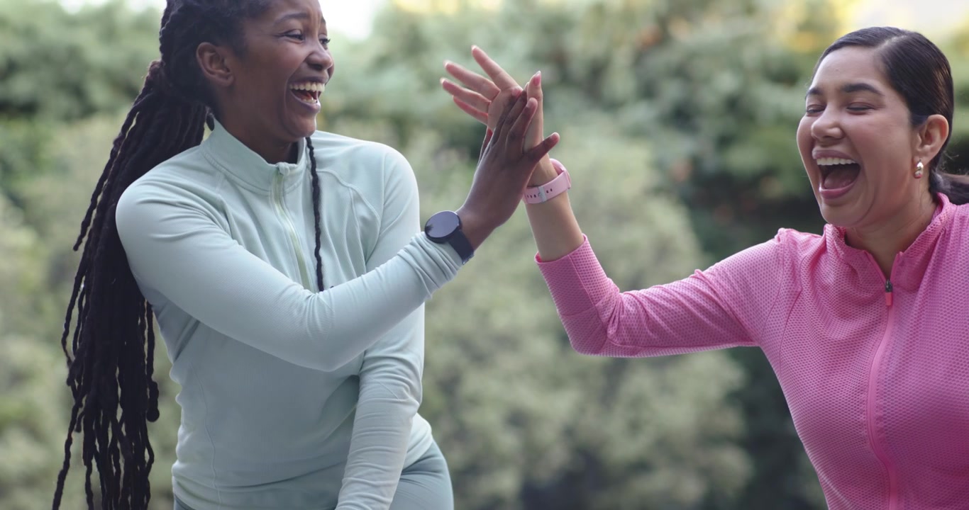 Diverse female friends following pink woman with watch, raising hand, helping friend stand in yard