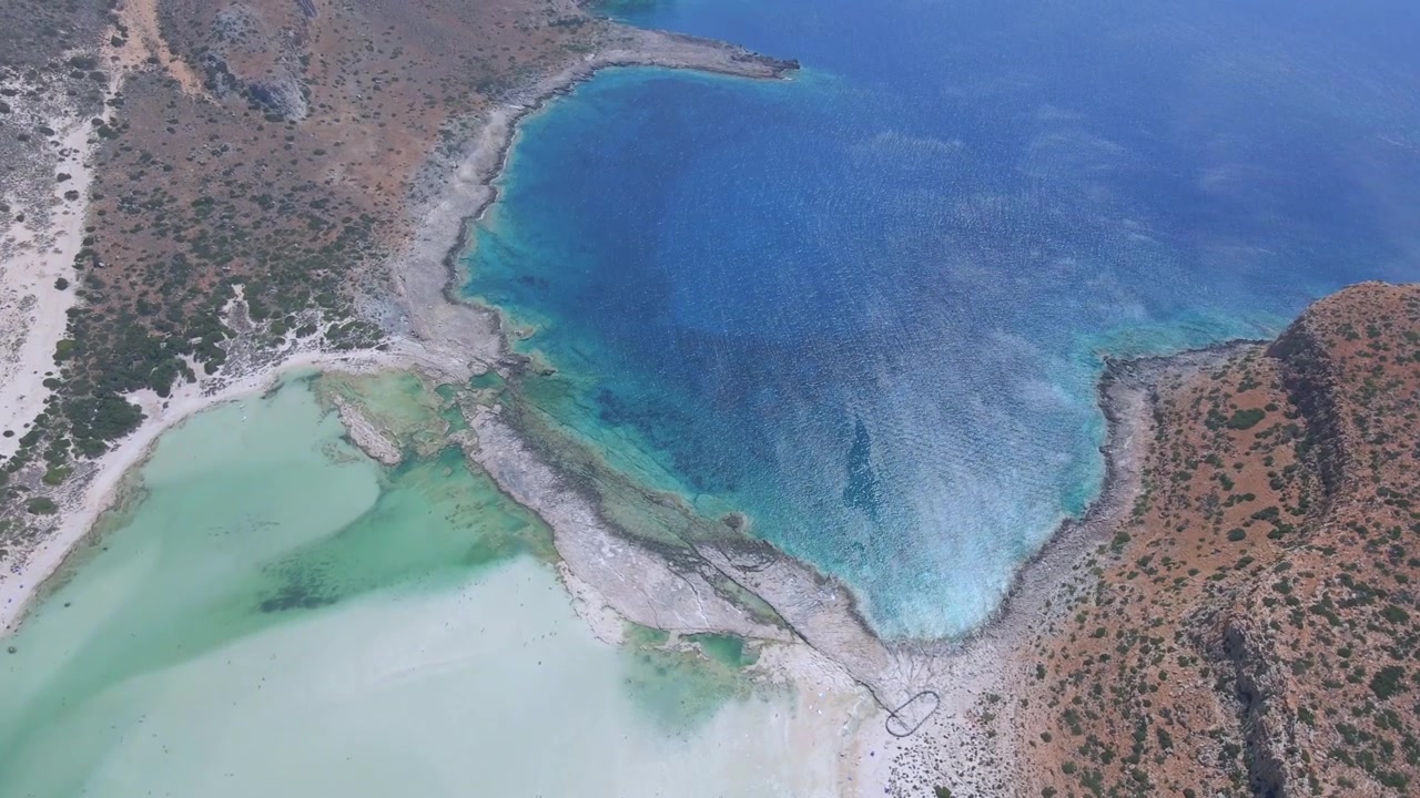 Spektakulär drönarbild från hög vinkel som fångar den dramatiska kontrasten mellan den grunda turkosa Baloslagunen och det djupblå havet på Kreta, Grekland. Vackert exotiskt kustlandskap, dagtid