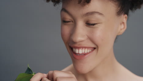 close up portrait beautiful mixed race woman smiling caressing face with leaf touching smooth healthy skin complexion enjoying natural skincare beauty on grey background