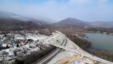 highway exist near a small town in winter snow, 60fps us to canada, ohio, arial drone shot, with mountains in the background