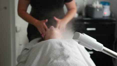 aesthetician beautician administering a facial treatment while a steam machine emits mist onto the client's face