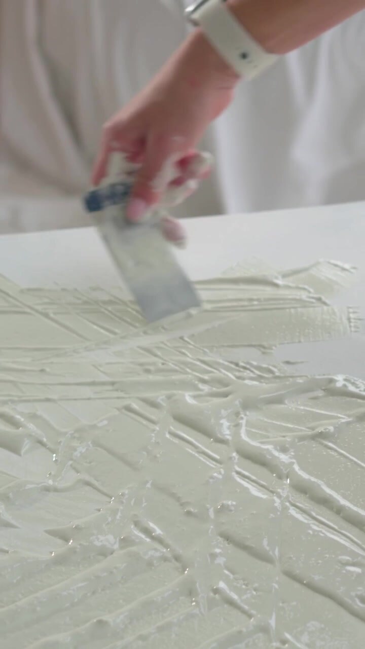 Woman spreading off-white gel, scraping with metal spatula and refining ridged texture for art