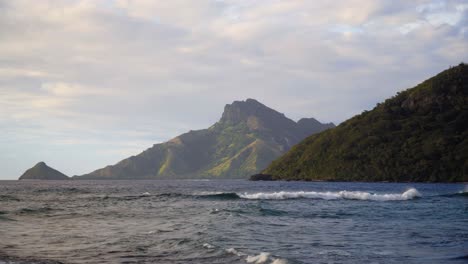 beautiful nature scenery of lush green mountains surrounded by the wavy blue ocean in an island in fiji on a sunny weather - medium shot