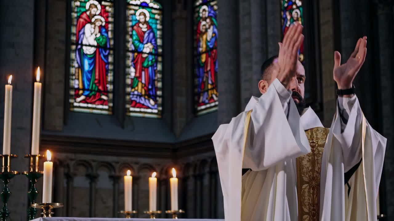 Kněz ve zdobeném rouchu stojí slavnostně v kostele, obklopen rozsvícenými svíčkami.