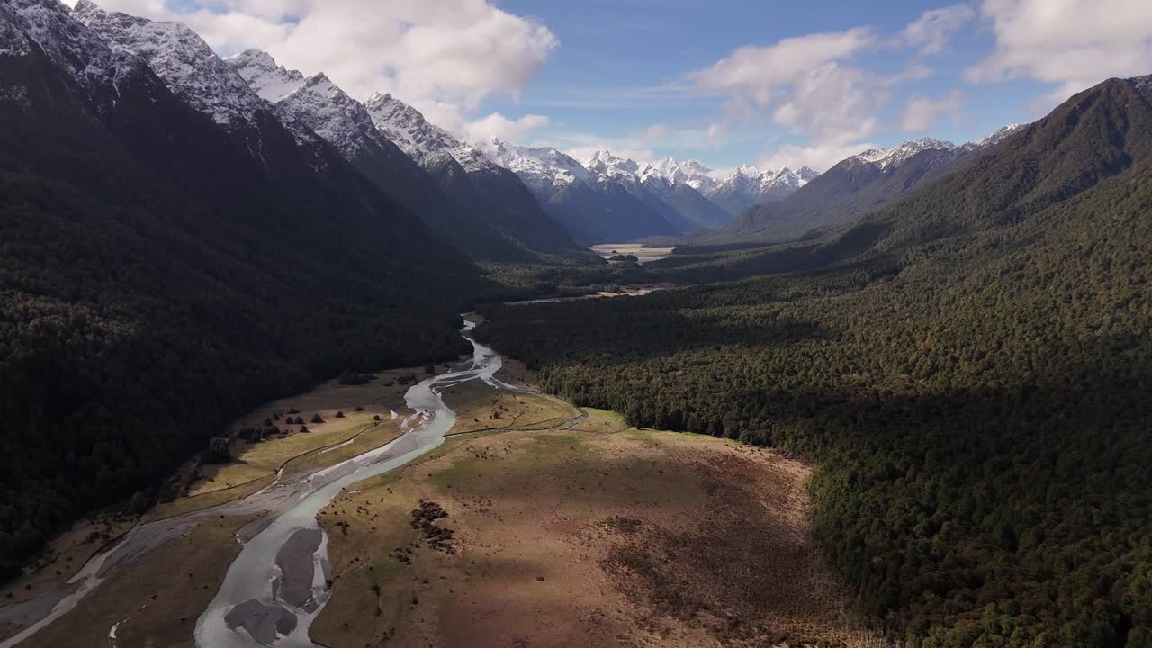 Ripresa aerea con drone che vola all'indietro sopra una valle fluviale, in direzione di Milford Sound. Maestose montagne innevate. Ideale per concetti epici di avventura e natura. Nuova Zelanda