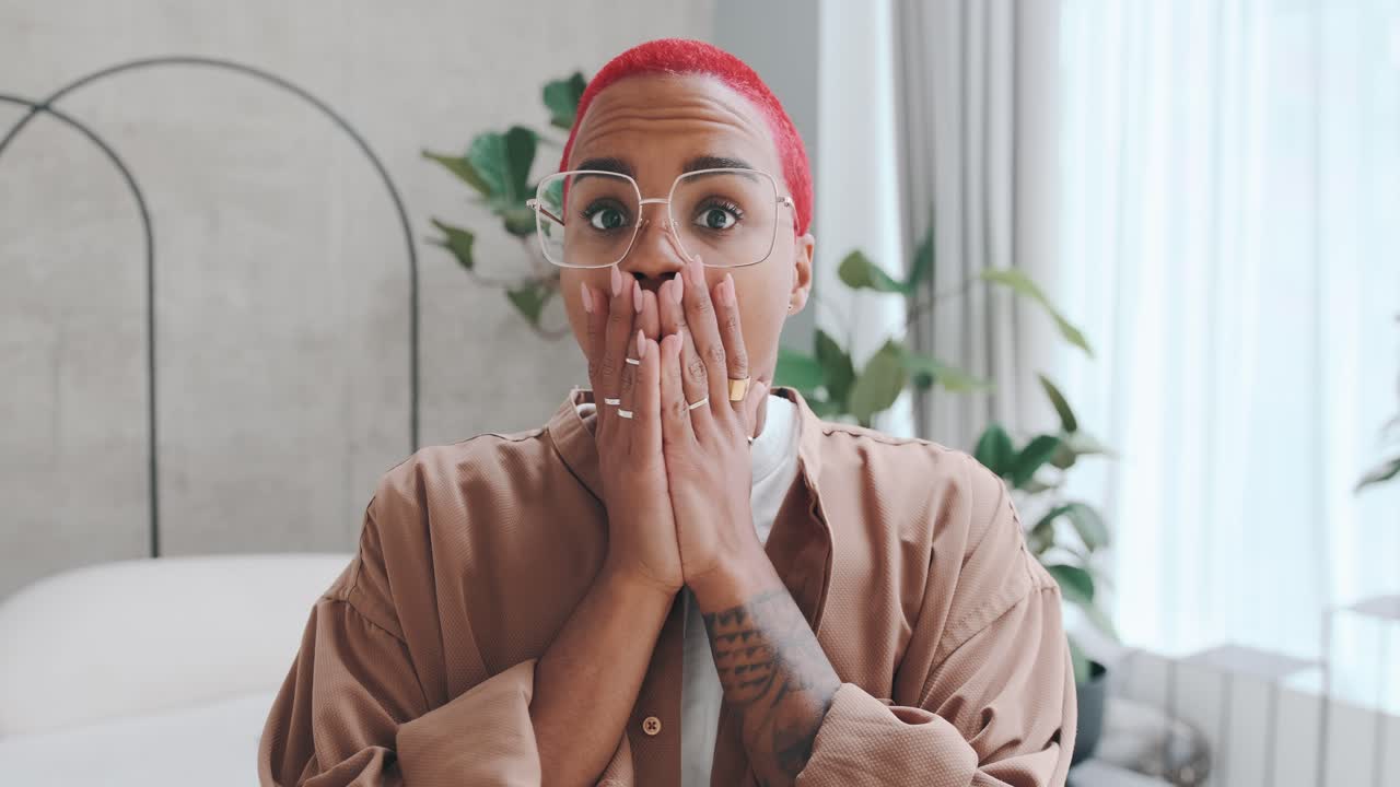 una joven afroamericana sorprendida cubre la boca abierta y agita la cabeza