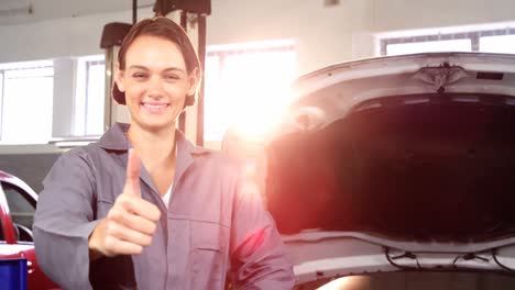 Female-mechanic-standing-in-repair-shop-showing-thumbs-up