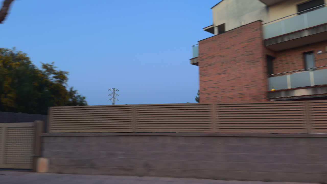 Modern suburban buildings and green landscape seen from moving car at sunset, showcasing urban life, architecture, travel, motion blur, and peaceful evening scenery