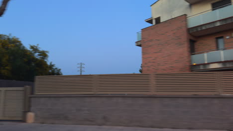modern suburban buildings and green landscape seen from moving car at sunset, showcasing urban life, architecture, travel, motion blur, and peaceful evening scenery