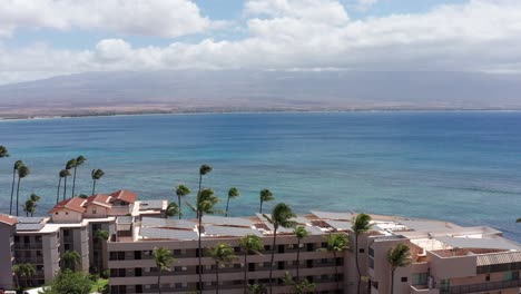 Aerial-low-panning-shot-of-Maalaea-Bay-behind-condos-with-Haleakala-in-the-distance-from-West-Maui,-Hawai'i