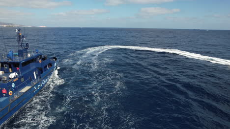 toma aérea de un bote patrullero de la policía y al lado del bote hay un bote que va a alta velocidad realizando operaciones