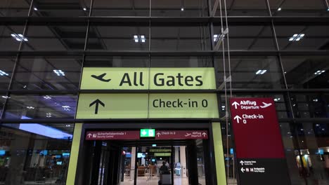 pov interior view of berlin brandenburg airport showing directional signage leading to all gates and check-in areas within the terminal building. tilt up shot