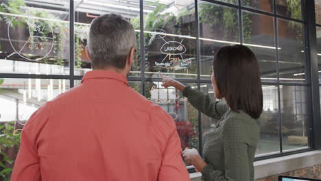 diverse male and female colleague brainstorming on glass wall in office, slow motion