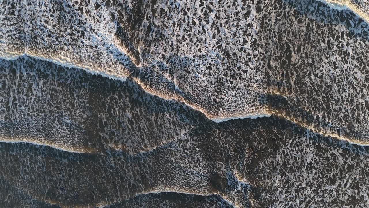 Birds eye view drone aerial view of north sea ocean waves crashing onto shore beach early morning sunrise seaburn beach sunderland england uk
