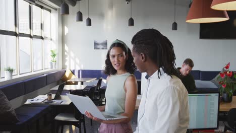 Diverse-business-people-discussing-work-and-using-laptop-at-office