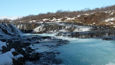 aerial view of brúarfoss waterfall in laugarvatn, haukadalur, iceland, featuring its striking blue waters cascading over dark volcanic rocks in a snowy winter landscape.