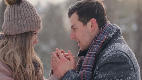 a caring man warms his wife's hands in the winter on the street in a snow-covered park.