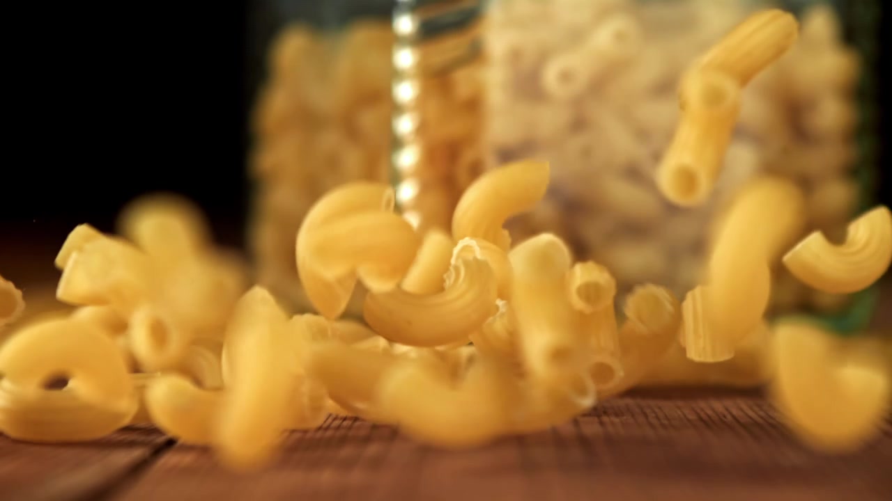 Rallentatore di pasta maccheroni secca che cade su un tavolo di legno