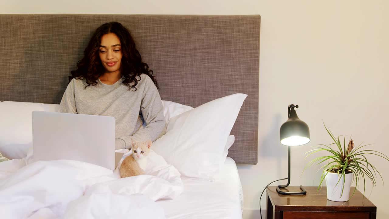 Donna che usa il suo laptop mentre è seduta sul letto con il suo gatto 4K.