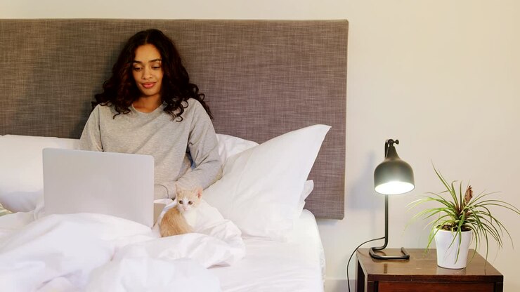 Kvinde bruger sin laptop, mens hun sidder på sengen med sin kat, 4K