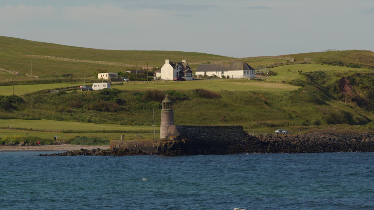 Wide shot of port Logan old lighthouse and harbour with buildings in background