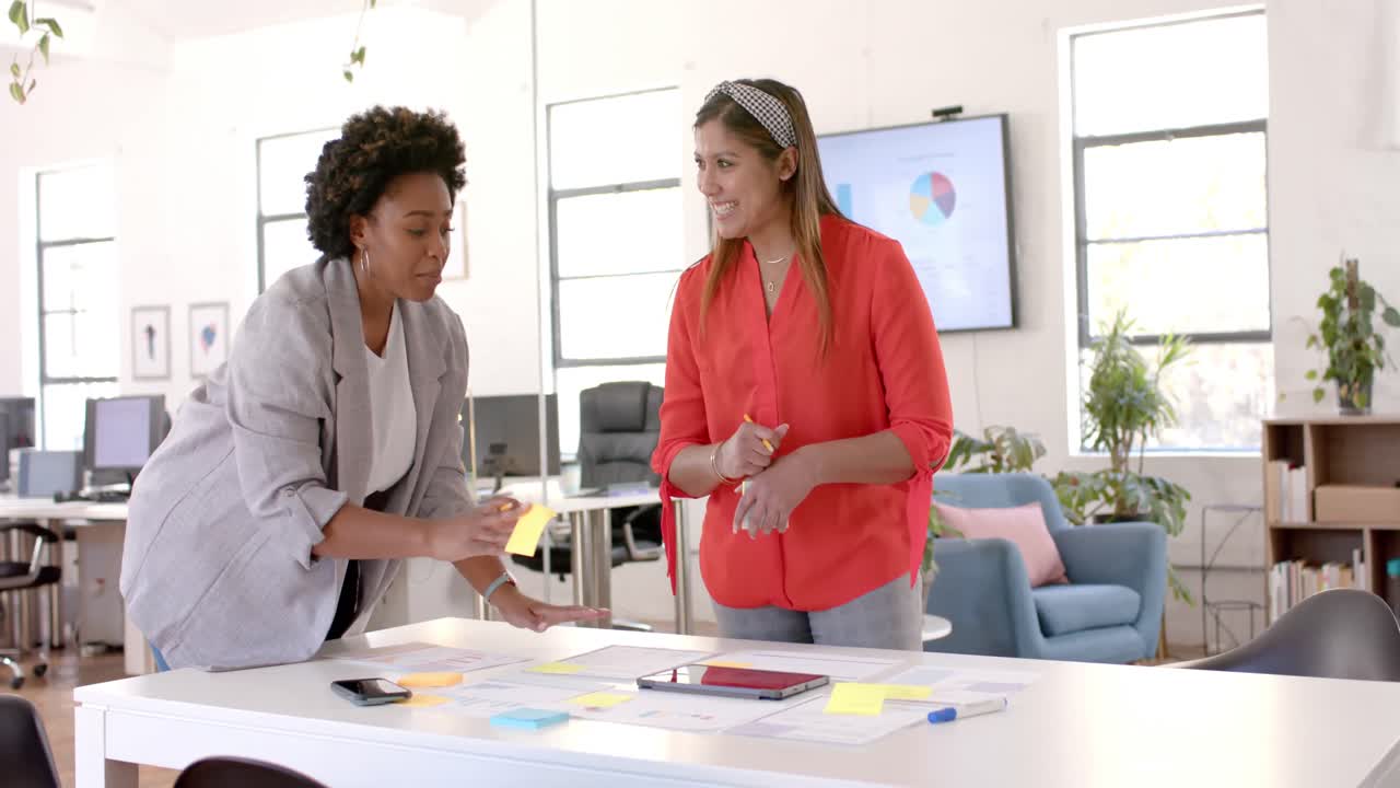 Diverse business female colleagues brainstorming using notes and tablet in office, slow motion