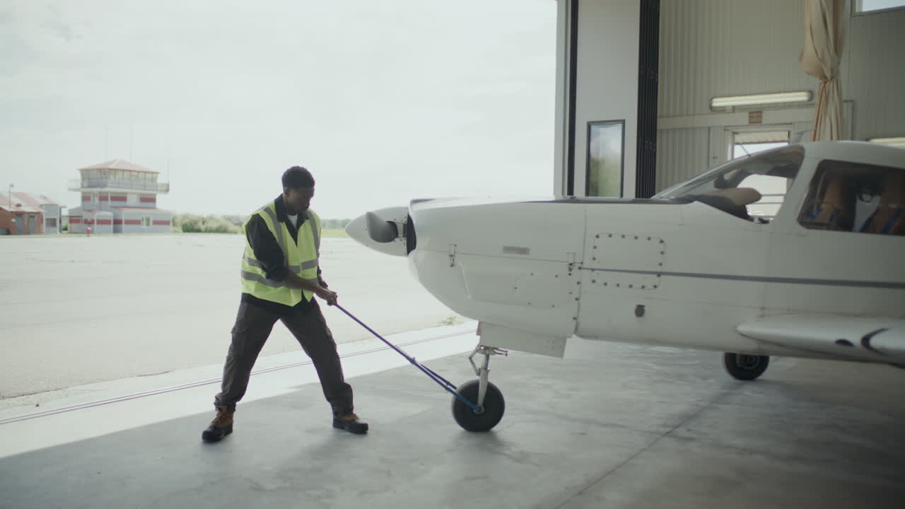 Ground Crew Member Moving Light Aircraft out of Hangar