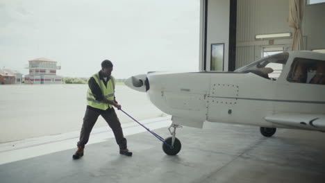 ground crew member moving light aircraft out of hangar