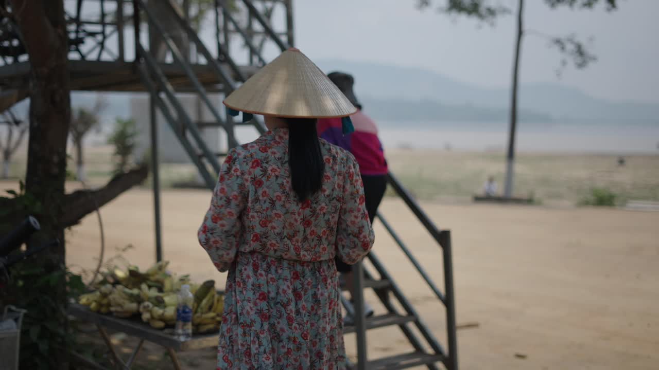 Woman at a riverside market wearing a traditional hat
