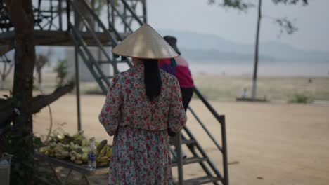 woman at a riverside market wearing a traditional hat