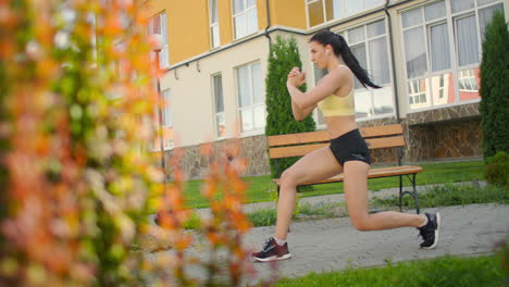 perform lunges in the city park against the background of buildings on the site. slow-motion foot training in headphones