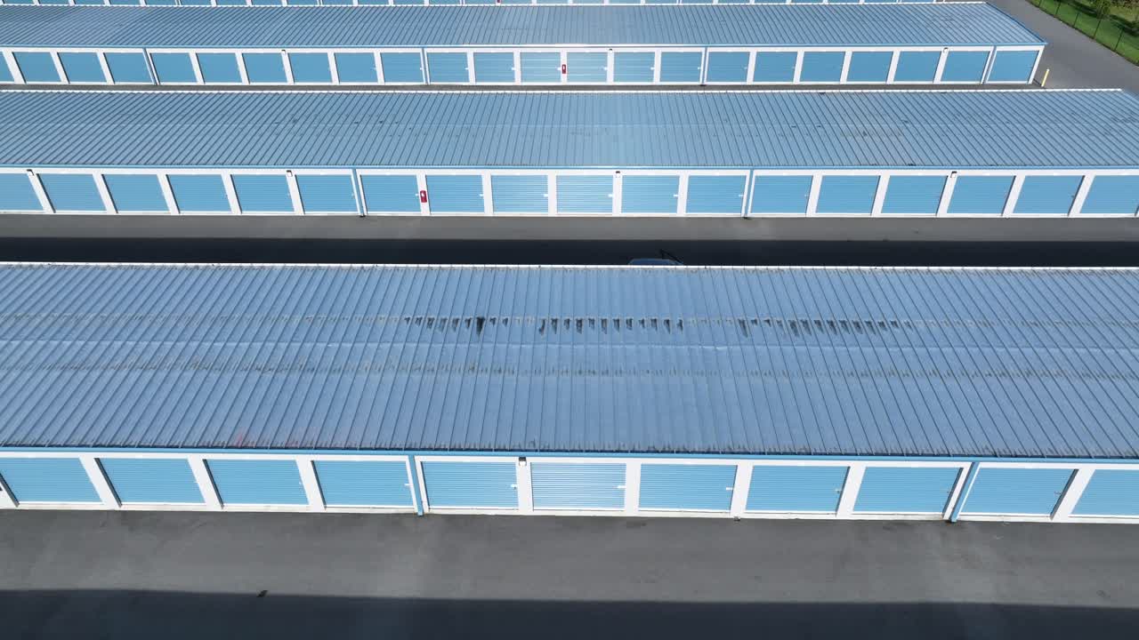 Row of blue colored self-storage unit buildings in american town. Sunny day in industrial area. Aerial lateral wide shot