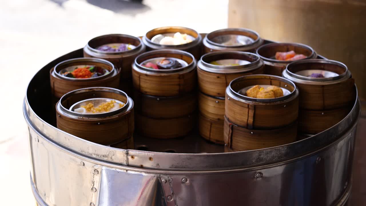 Hands arranging bamboo steamers filled with dim sum on a metal steamer in a market setting