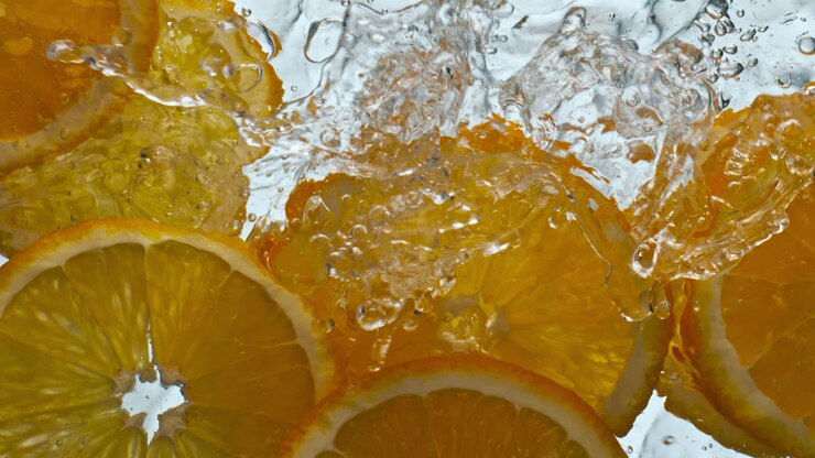 Primo piano: fette d'arancia che schizzano acqua in super slow motion. Agrume che galleggia.