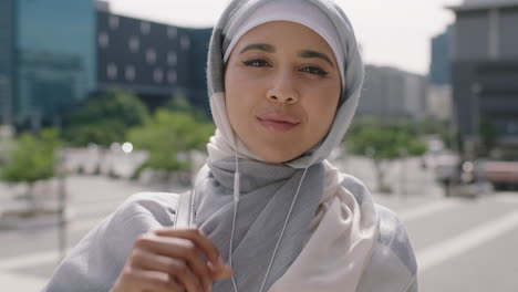 portrait of beautiful young muslim woman student looking confident at camera listening to music using earphones wearing hajib headscarf