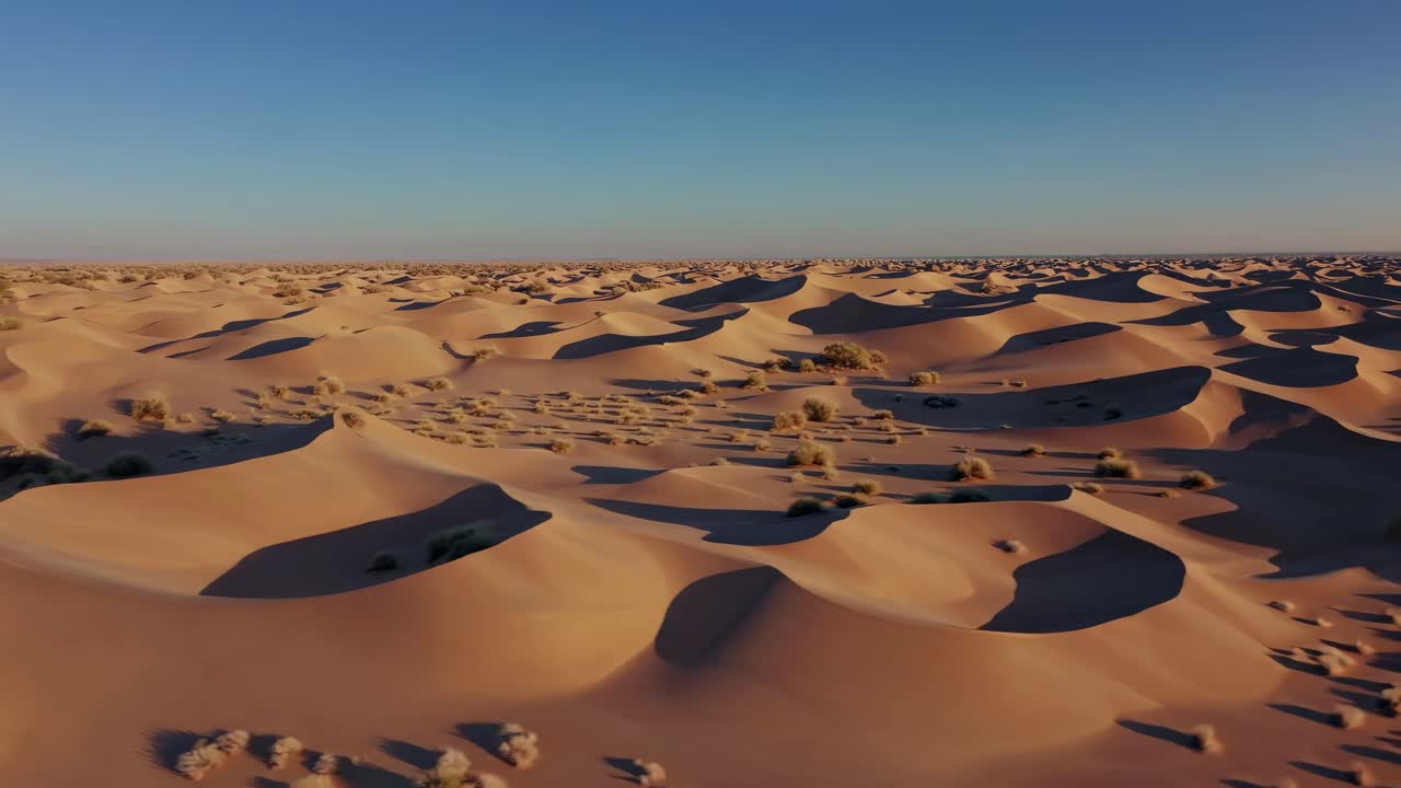 Aerial video captures vast desert dunes at sunset, highlighting their curves and shadows